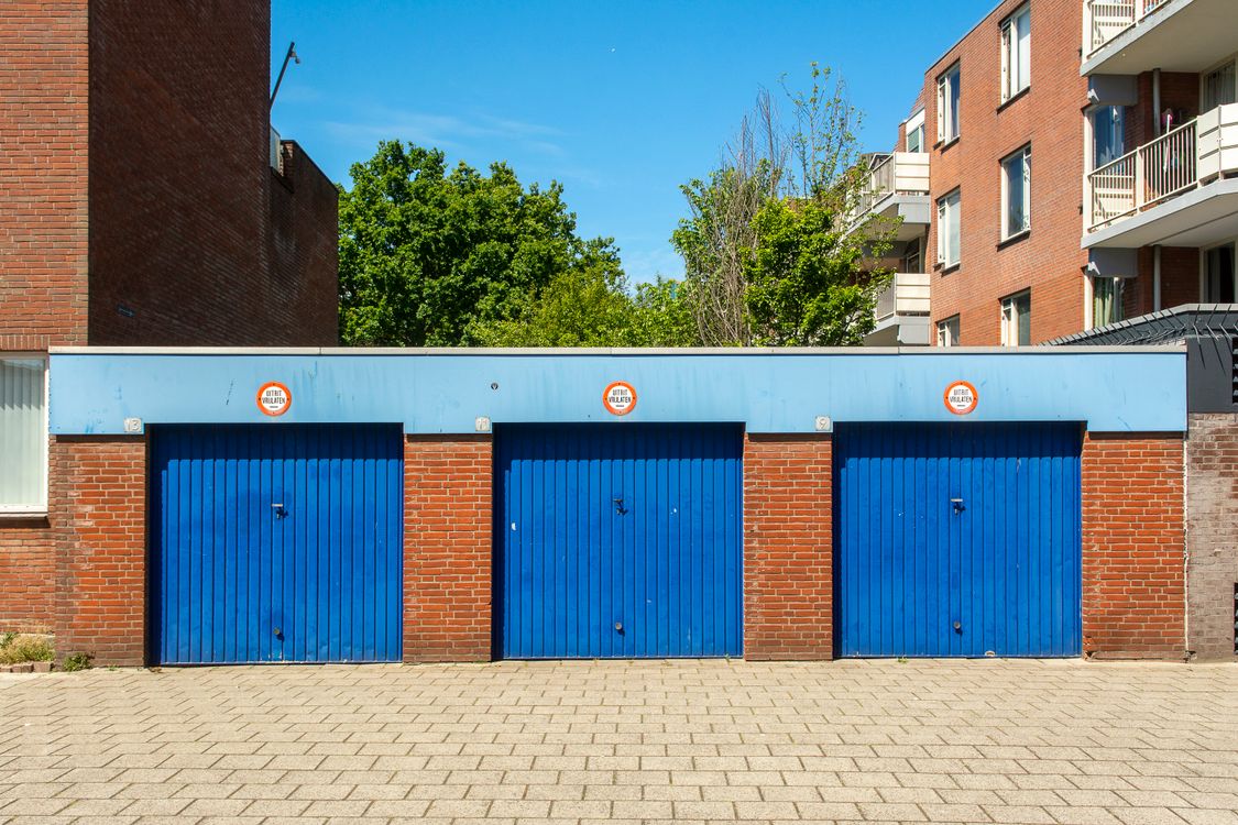 Three blue residential garage doors on a brick building.