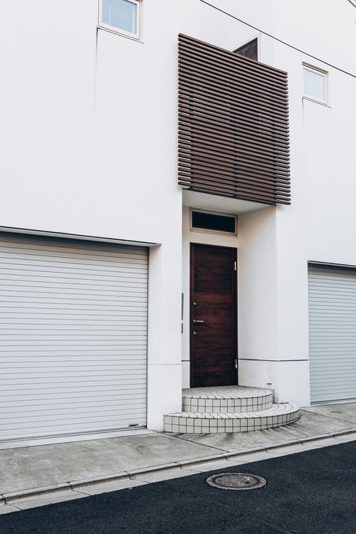 White building facade with wooden door and twin garage entrances.