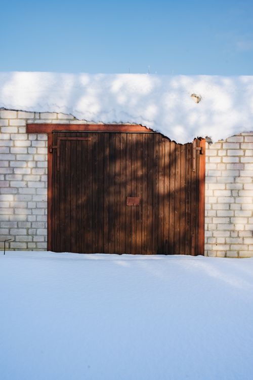 Wooden garage door framed by brick walls under a clear blue sky with fresh snow.