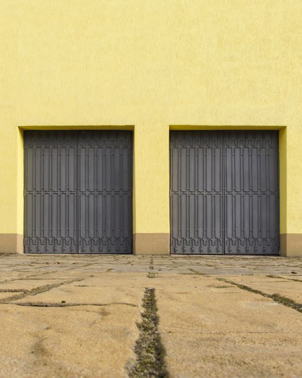 Yellow wall with two closed grey garage doors.